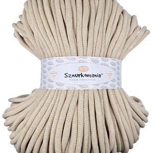 Könnte beinhalten: Ein Ball aus beigefarbenem Baumwollgarn, mit einem Etikett mit der Aufschrift "Sznurkomania Pasja tworzenia" (polnisch für "Cord Mania Passion for Creation").