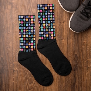 May include: A pair of black socks with a colorful pattern of cryptocurrency logos. The socks are on a wooden surface.
