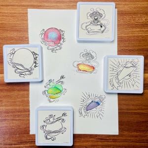 May include: Set of eight white square rubber stamps with black ink designs of bottles and swirls. The stamps are on a white sheet of paper on a wooden surface. The designs include a bottle with a heart, a bottle with a star, a bottle with a swirl, a bottle with a crescent moon, a bottle with a sun, a bottle with a rainbow, a bottle with a cloud, and a bottle with a star.