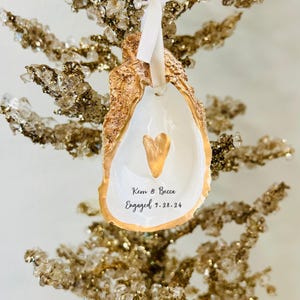 May include: Gold oyster shell ornament with a gold heart and the text "Kern & Becca Engaged 7.28.24".
