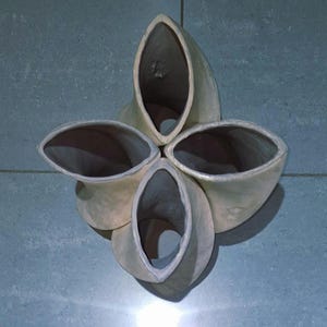 May include: A cream-colored, four-part wall sculpture with a flower-like design. Each section has an oval opening and a textured surface. The sculpture is mounted on a blue-gray tiled wall.