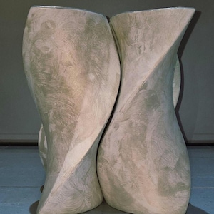 May include: Two abstract, light-colored sculptures with a textured, swirling pattern. The forms are tall and slender, with a slight twist in their design. The sculptures are placed close together, creating a sense of unity and artistic expression.