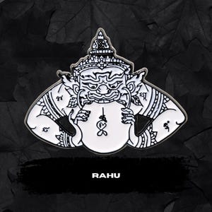 May include: A white and black enamel pin featuring a stylized depiction of Rahu, a figure from Thai mythology. The pin has intricate details and the word "RAHU" in a bold font at the bottom.