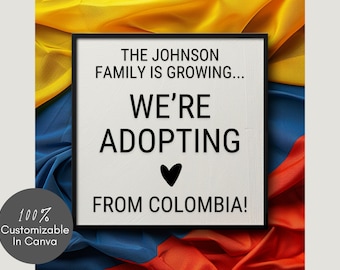 May include: A white sign with black text announcing "The Johnson Family is Growing... We're Adopting from Colombia!" with a black heart symbol. The sign is framed in black and is set against a background of yellow, blue, and red fabric.