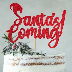 May include: Red glitter cake topper with the text "Santa's Coming!" on a white frosted cake with green sprigs and red berries.