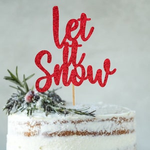Peut inclure: Un gâteau blanc avec un topper de gâteau rouge pailleté qui dit "Let it Snow". Le gâteau est décoré de brins de romarin et d'une poussière de sucre glace.
