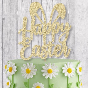 May include: Gold glitter cake topper with the words "Happy Easter" and bunny ears. The topper is on a green cake decorated with white daisies.
