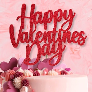 Peut inclure: Un gâteau rose décoré de glaçage rose et rouge et de bonbons en forme de cœur. Un topper de gâteau rouge pailleté indique "Happy Valentines Day".