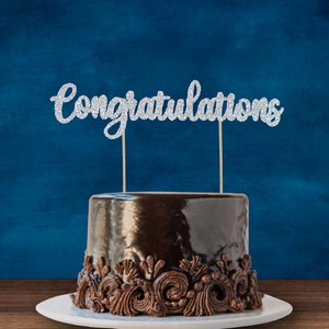 May include: A chocolate cake with a silver glitter "Congratulations" cake topper.