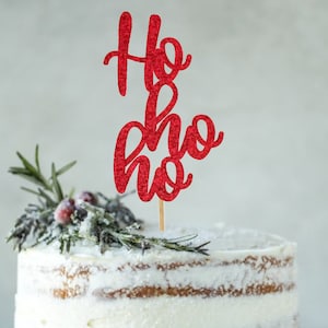 Op de afbeelding: Een witte cake met een rode glitter "Ho Ho Ho" caketopper en een takje rozemarijn met rode bessen.