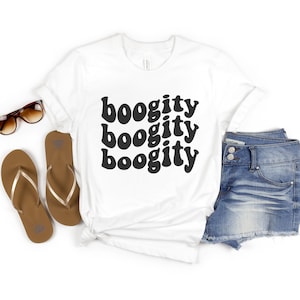 May include: White t-shirt with the text "boogity boogity boogity" in black, retro-style font. The shirt is laid out on a white background with a pair of brown flip-flops and blue denim shorts.