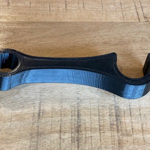 K&ouml;nnte beinhalten: Ein schwarzes Plastikwerkzeug mit zwei Schlaufen an beiden Enden. Das Werkzeug ist zum &Ouml;ffnen und Schlie&szlig;en von Flaschenverschl&uuml;ssen gedacht.