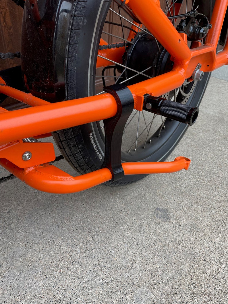 K&ouml;nnte beinhalten: Nahaufnahme eines orangefarbenen Fahrradrahmens mit einem schwarzen Fu&szlig;tritt und einem schwarzen Reifen mit der Aufschrift "POWERBIKES" auf der Seite.