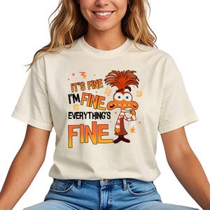 May include: A white t-shirt with a cartoon character holding a cup of coffee. The text on the shirt reads "It's fine I'm fine Everything's fine".
