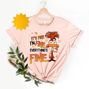 May include: Pink t-shirt with a cartoon character and the text "It's fine I'm fine Everything's fine".