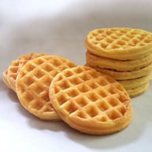 以下が含まれることがあります： 黄金色のワッフルの積み重ね。手前に単体のワッフルがいくつかある。ワッフルは、クラシックな正方形の格子模様になっている。