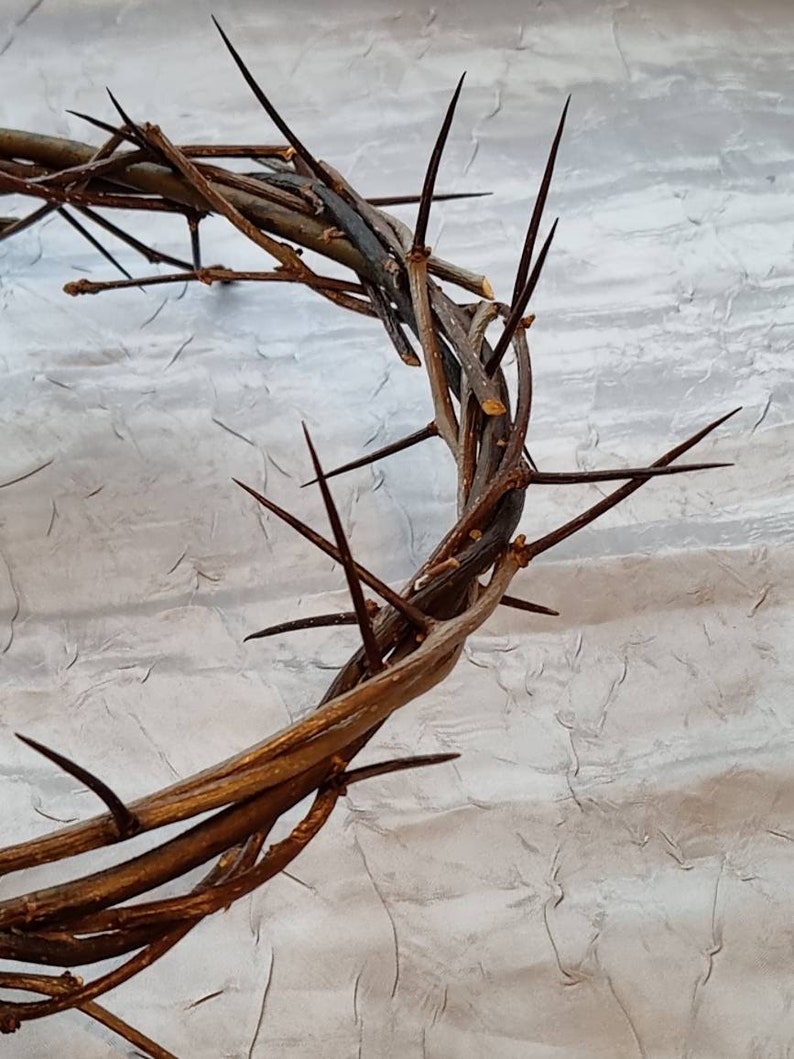 May include: A brown woven crown of thorns with sharp black thorns. The crown is on a white textured background.