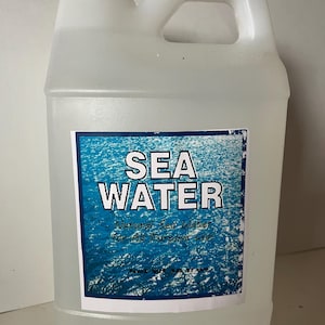 Könnte beinhalten: Ein durchsichtiger Plastikkanister mit weißem Deckel, gefüllt mit Meerwasser. Das Etikett lautet "SEA WATER Natural Sea Water for All Purposes".