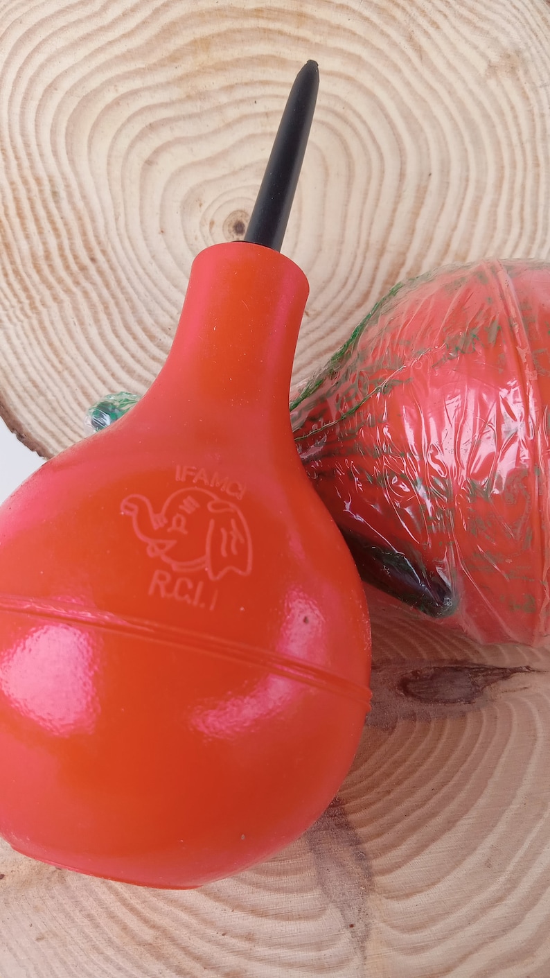 May include: A red rubber bulb air blower with a black nozzle. The bulb has a white elephant logo with the text "IFAMO R.C.I."