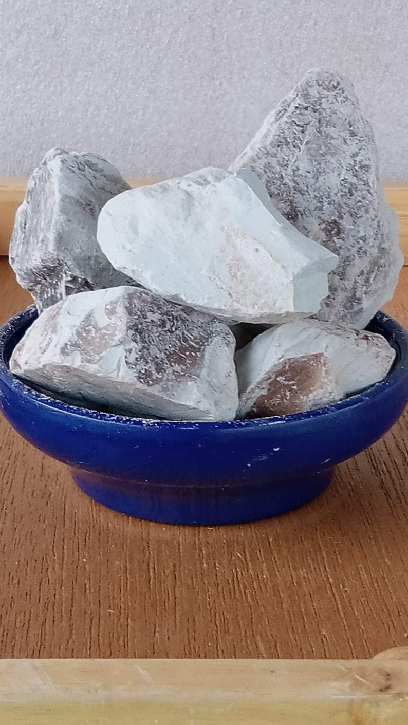 K&ouml;nnte beinhalten: Eine Sammlung hellblauer und grauer Steine, m&ouml;glicherweise Mineralien oder Kristalle, wird in einer kleinen, tiefblauen Keramikschale pr&auml;sentiert. Die Steine haben eine raue, strukturierte Oberfl&auml;che und verschiedene Farbt&ouml;ne. Die Schale steht auf einer Holzoberfl&auml;che.