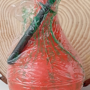 May include: A red rubber bulb with a black handle, wrapped in clear plastic with green markings. The bulb is sitting on a wooden surface.