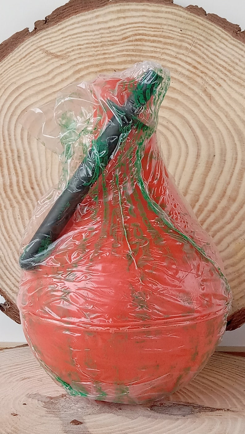 May include: A red rubber bulb with a black handle, wrapped in clear plastic with green markings. The bulb is sitting on a wooden surface.