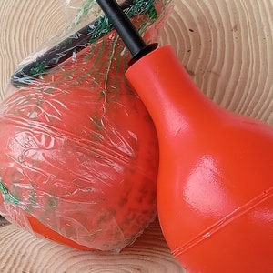May include: Two red rubber bulb syringes with a black nozzle. The syringes are on a wooden surface.