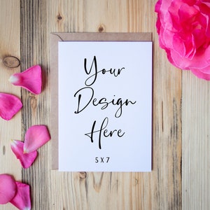 May include: A white card with the text "Your Design Here" and "5x7" printed on it. The card is on a wooden surface with pink rose petals scattered around it.