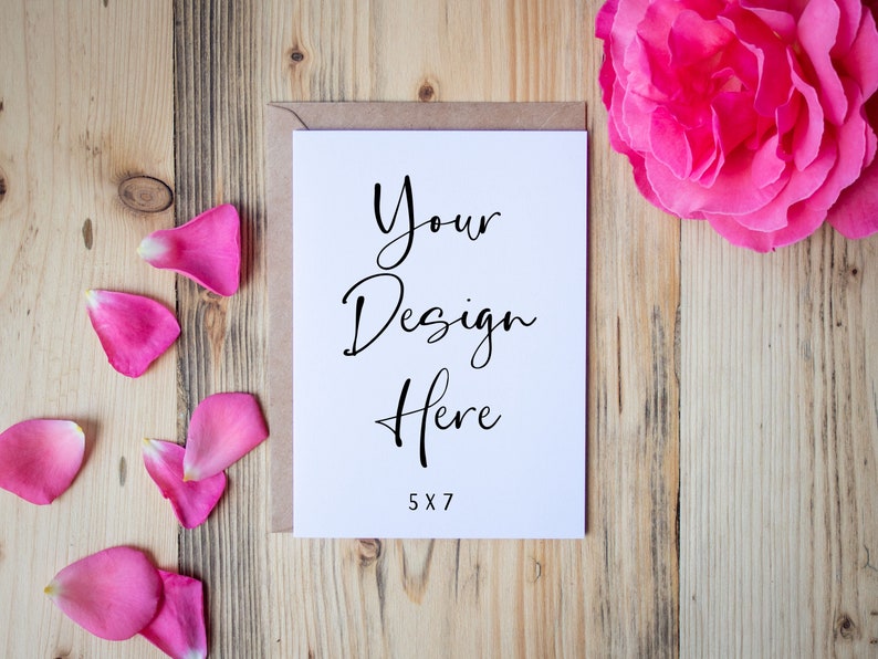 May include: A white card with the text "Your Design Here" and "5x7" printed on it. The card is on a wooden surface with pink rose petals scattered around it.