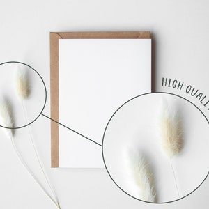 May include: A blank white card with a brown envelope on a white background. Two white fluffy stems are on either side of the card.