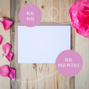 May include: A white card with a blank space for writing, surrounded by real rose petals and a real rose. The text "REAL ROSE" is written on a pink circle above the card and the text "REAL ROSE PETALS" is written on a pink circle below the card.
