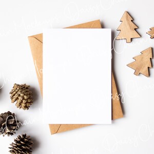 K&ouml;nnte beinhalten: Eine leere wei&szlig;e Karte mit einem braunen Umschlag, Tannenzapfen und h&ouml;lzernen Weihnachtsbaumschmuck auf wei&szlig;em Hintergrund.