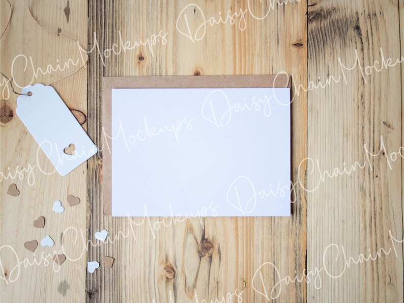 May include: A blank white card with a brown envelope on a wooden background. There are small white and brown hearts scattered around the card.