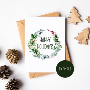 K&ouml;nnte beinhalten: Eine wei&szlig;e Karte mit einem gr&uuml;nen Aquarellkranz mit roten Beeren und dem Text "Happy Holidays". Die Karte ist von Tannenzapfen und Holz-Weihnachtsb&auml;umen auf wei&szlig;em Hintergrund umgeben.