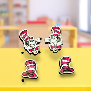May include: Four wooden earrings featuring the Cat in the Hat character from the book by Dr. Seuss. The earrings are painted in red, white, and black.