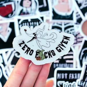 May include: White vinyl sticker with a black and white illustration of a character from the Nightmare Before Christmas movie. The character is flying with a spider web behind it. The text "Zero Fcks Given" is written around the character in a black font.