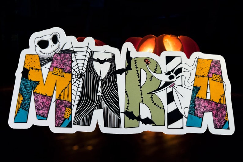 May include: A colorful, patchwork-style name sign that reads "MARIA" with a Jack Skellington character from the Nightmare Before Christmas movie. The sign is decorated with bats, spiderwebs, and other Halloween-themed elements.