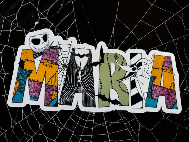 May include: A white sticker with the name "MARIA" written in colorful patchwork letters. The letters are decorated with black and white stripes, spiderwebs, and a cartoon character with a stitched mouth.
