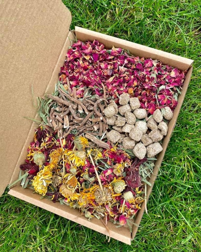 May include: A cardboard box filled with dried herbs and flowers for small animals. The box contains dried rose petals, dried calendula flowers, dried herbs, and small brown pellets.