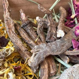 May include: A close-up of a mix of dried herbs and flowers, including dried roots, petals, and leaves. The mix is a light brown color with hints of yellow and pink.