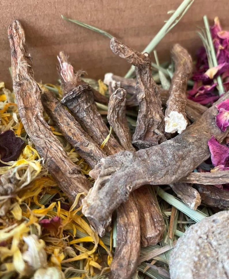 May include: A close-up of a mix of dried herbs and flowers, including dried roots, petals, and leaves. The mix is a light brown color with hints of yellow and pink.