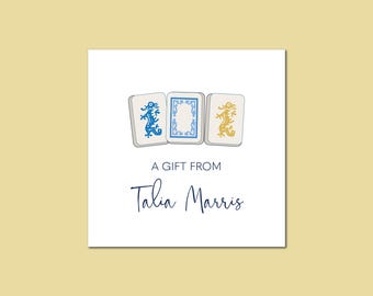 May include: A white gift tag with three blue and white mahjong tiles featuring a gold dragon design. The text "A gift from Talia Marris" is printed in blue.