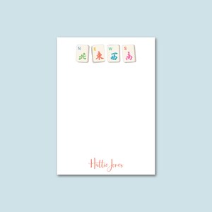 May include: White notepad with a red, blue, green, and yellow design of Chinese mahjong tiles spelling out the word "NEWS". The name "Hattie Jones" is written in red cursive at the bottom of the notepad.