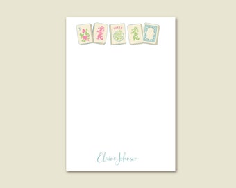 May include: A white notepad with a blue and green border of mahjong tiles. The tiles have Chinese characters and the word "Joker" on them. The notepad has the name "Elaine Johnson" written in blue cursive at the bottom.