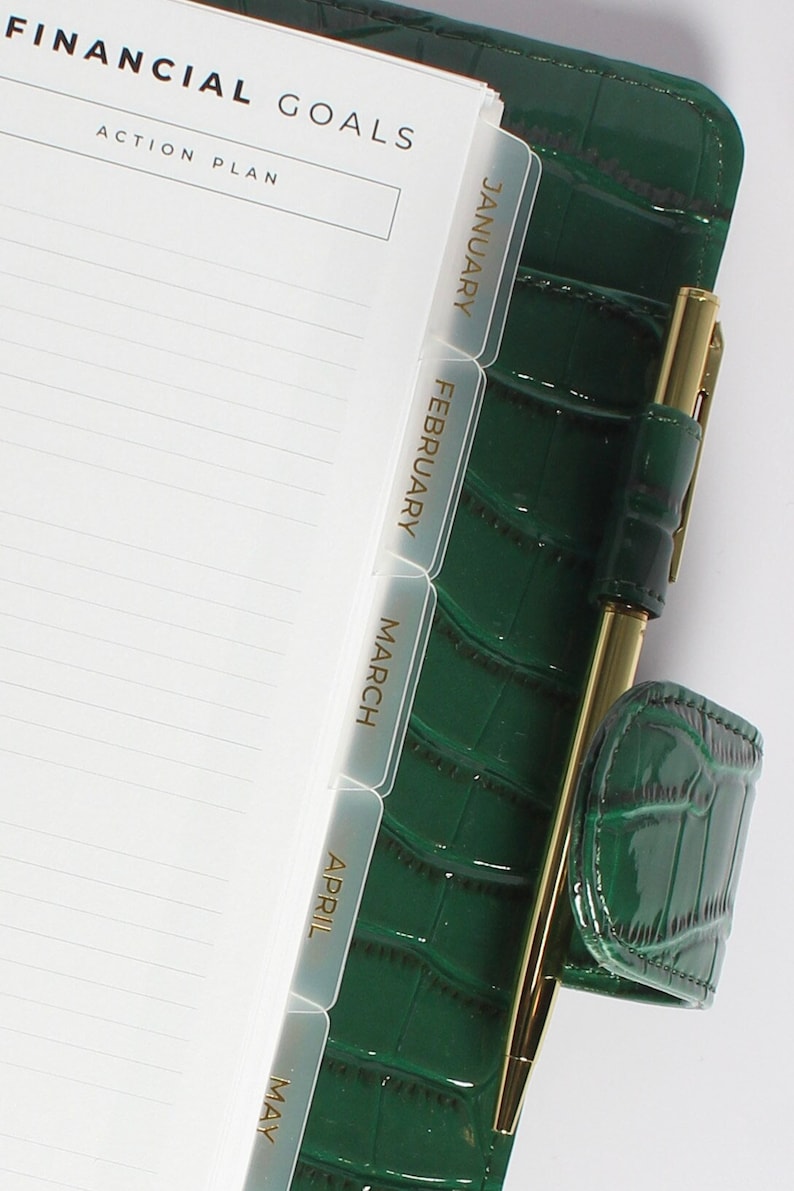 May include: A green faux leather planner with gold accents and clear plastic tabs labeled January through May. The planner has a pen holder and a pen with a gold clip.