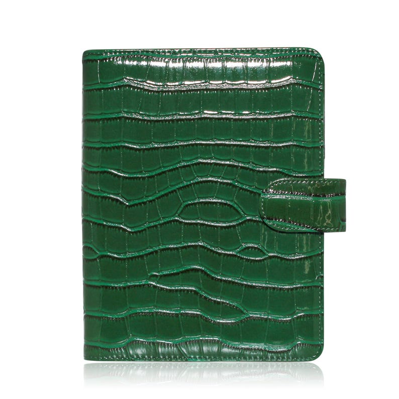 May include: A glossy, emerald green organizer with a crocodile skin texture. The cover has a rectangular shape with rounded corners and a flap closure on the right side. The surface reflects light, highlighting the embossed pattern.