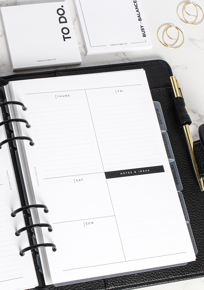 Op de afbeelding: Een zwarte lederen agenda met een witte pagina opengeklapt naar een wekelijkse lay-out. De pagina is verdeeld in secties voor donderdag, vrijdag, zaterdag en zondag. De agenda heeft een zwarte metalen binding en bevat tabbladen voor augustus, september en oktober. De agenda heeft ook een sectie voor notities en idee&euml;n.