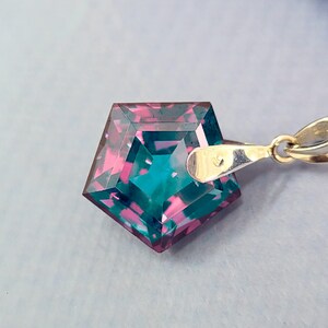 May include: A silver necklace featuring a pendant with a geometric, pentagon-shaped gemstone. The gemstone displays a blend of teal and magenta hues. The chain is delicate and the pendant is attached with a small clasp.