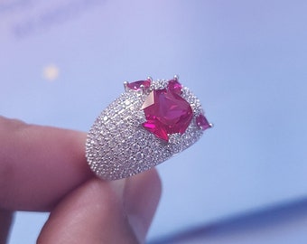 May include: A silver ring featuring a large red gemstone surrounded by smaller red gemstones and a band of small white gemstones.