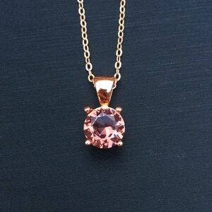 Puede incluir: Un delicado collar de cadena dorada con un colgante redondo de piedra preciosa rosa.
